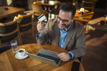 Man celebrating online shopping success holding credit card and laptop