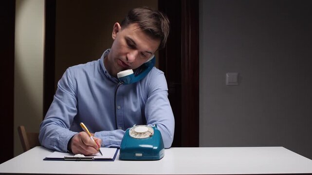 Man noting telephone, Man recording call details, Individual jotting notes during phone conversation, Individual balancing recording notes while engaged in telephone call using traditional tools