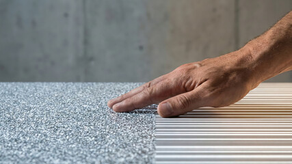 Hand touching textured flooring sample with modern striped tile transition, tactile contrast and neutral palette