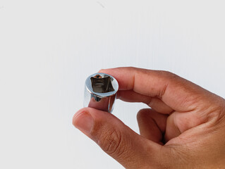 A human hand holding a chrome socket wrench head against a clean white background, illustrating manual grip, mechanical tools, and practical industrial or repair work.