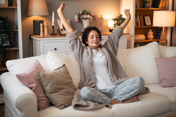 Obraz premium Relaxed Woman Stretching on White Sofa in Cozy Living Room With Pajamas
