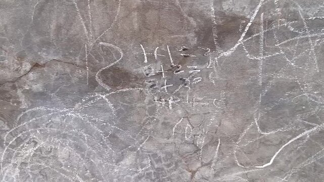 Close-up of a weathered grey concrete wall covered in intricate abstract white chalk markings and natural cracks