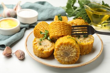 Pieces of boiled corn cobs with parsley served on white table, closeup