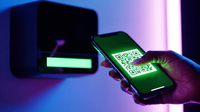 A smartphone displays a green QR code as a hand holds it near a black box with a red light on the wall