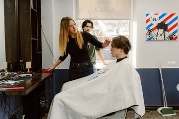 A stylist carefully works on a young man's hair at a modern salon. The vibrant décor and natural light create a welcoming atmosphere, enhancing the grooming experience enjoyed by the client.
