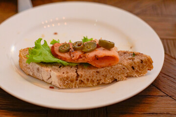 Side view of smoked salmon open sandwich with lettuce and jalapeno on rustic seeded bread, served on a white plate. Gourmet brunch and café food concept