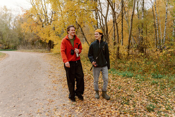 Fototapeta premium Two friends stroll down a winding path surrounded by bright autumn leaves. They share laughter and stories, enjoying the warmth of the sun and the beauty of nature.
