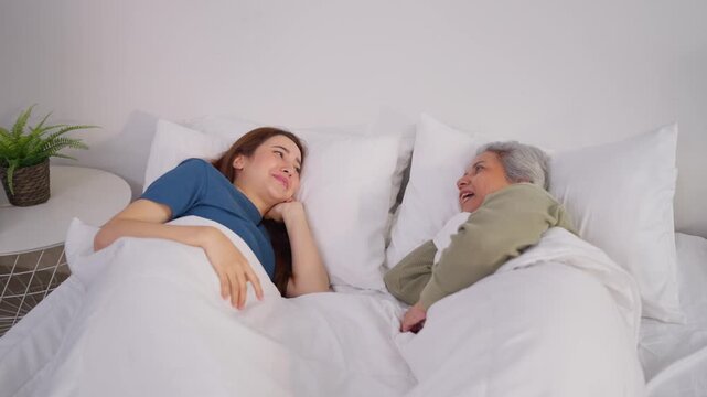 Asian senior mom and daughter lying down on bed in bedroom at home in morning.