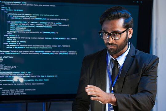 An Indian male software engineer or team lead discusses Python code for an AI algorithm. A developer in the audience raises their hand to ask a technical question during a code review. - Powered by Adobe