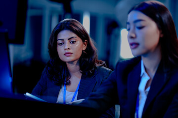 Late night code warriors: Two female developers intensely debugging code together, eyes locked on the screen, determined to solve a complex issue before the product launch.