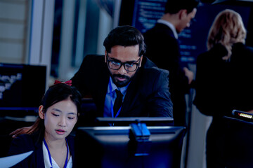 Intense collaboration hub Diverse AI team deep dive into project data late night. Manager guides Asian colleagues reviewing analytics for a new service launch in tech office.