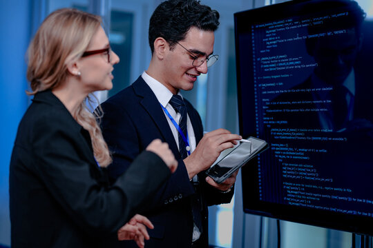 Intense code walkthrough. A female developer uses a stylus pointing to a specific line of code on the screen explaining its function to her male teammate during a debugging session.