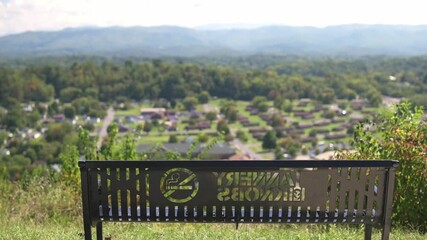 bench overlooking suburban town mountains, sunny afternoon empty memorial bench engraved plaque distant blue ridgeline lush green canopy quiet atmosphere gentle breeze panoramic vista