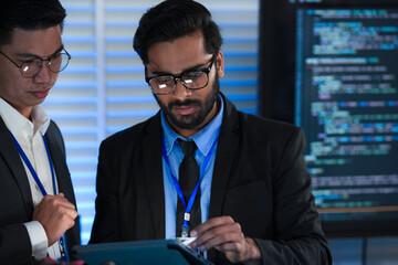 Lead developers analyze system architecture late night using tablet stylus pointing out details colleagues focused code visible screens debugging technical deep dive software build.