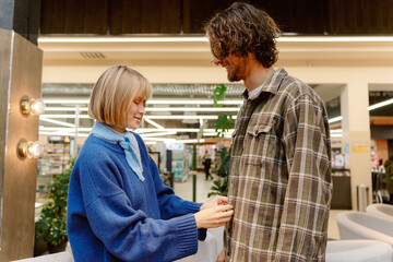 Fototapeta premium In a bright, trendy location, a couple enjoys a sweet interaction. The woman is fastening a button on the man's flannel shirt, creating a cozy atmosphere of affection and connection.