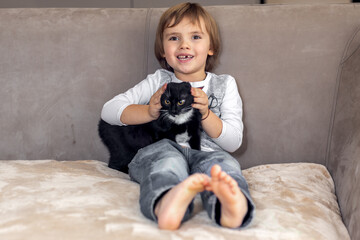 Boy playing with black kitten on sofa at home