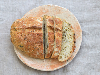 Top view of a sliced multigrain sourdough bread loaf on a ceramic plate. Crusty exterior and airy crumb texture shown in natural light on neutral linen fabric.