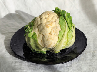 Fresh whole cauliflower head on black ceramic plate in natural light, organic vegetable still life for healthy cooking and clean eating concepts. healthy cooking, plant-based ingredients, clean eating
