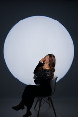 Elegant studio portrait of a glamorous woman wearing a black dress and holding black flowers, photographed against a dramatic circular spotlight background.