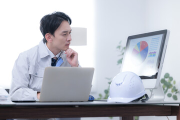 現場事務所で考える作業着の作業員　発注や下請けで納期に困るや経営などの戦略を考える