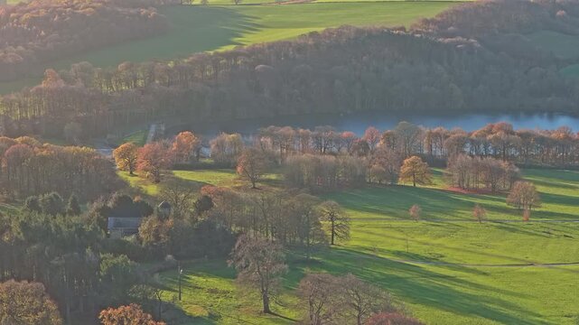 Aerial view of the tranquil Bretton Lake and surrounding dense autumnal woodland within the scenic and the serene environment of the Yorkshire Sculpture Park in West Yorkshire, UK.