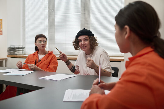 Three young adult women sitting at table discussing educational materials in classroom setting during prison education program