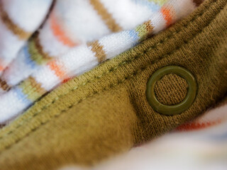 Close up shot of a white fabric with line pattern and an olive green binding with a circle snap button.