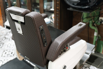 Vintage-style barber chair with brown leather cushion in a classic barbershop interior featuring patterned tile flooring and grooming tools.