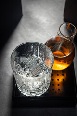 Premium Crystal Old Fashioned Glass with Clear Ice Cube and Whiskey Decanter on Dark Mood Lighting