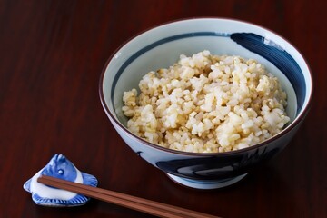 Close up shot of freshly cooked brown rice in traditional Japanese rice bowl with wooden chopsticks on wooden table.