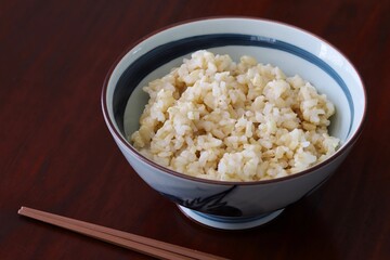 Close up shot of freshly cooked brown rice in traditional Japanese rice bowl with wooden chopsticks on wooden table.