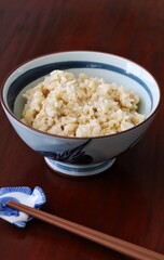 Close up shot of freshly cooked brown rice in traditional Japanese rice bowl with wooden chopsticks on wooden table.
