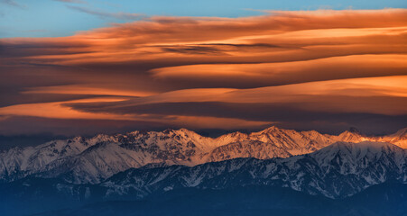 A picturesque landscape with lenticular clouds over the Trans-Ili Alatau mountain range near the Kazakh city of Almaty on a spring evening at sunset.
