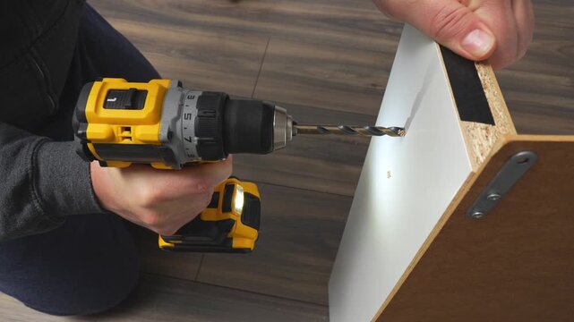 Individual using power drill to create holes in wooden panel, showcasing step-by-step drilling process with visible tool and material interaction