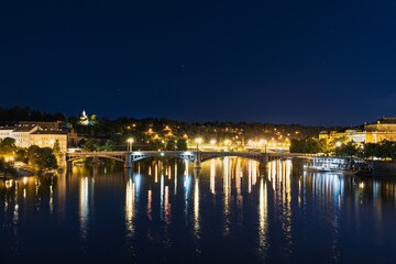 Obraz premium Experience the enchantment of Prague, Czech Republic at night with a breathtaking view of the Vltava River. The illuminated bridge and city lights reflect beautifully on the water.