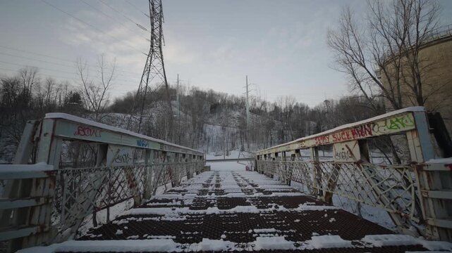 Belgo factory abandoned bridge in Shawinigan Quebec Canada with camera pushing forward over snow covered metal walkway, graffiti railings and winter industrial ruins