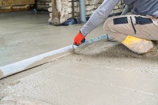 A skilled craftsman levels a concrete floor with a hand trowel, ensuring a smooth surface. Ideal for illustrating construction, renovation, and home improvement projects.