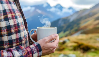 Close up of hands holding a steaming cup of coffee or tea with a stunning view of snowy mountains in the background