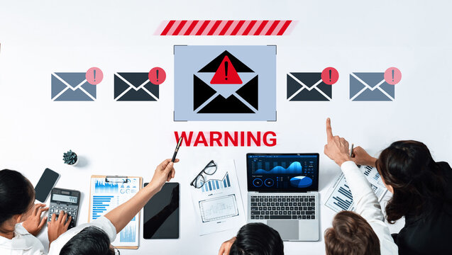 A group of business professionals engaged in a meeting about email security threats. They analyze data on laptops, with a warning email displayed on the screen. Gantry - Powered by Adobe