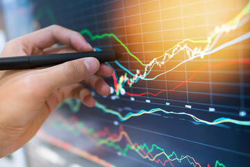Analyzing financial data with a stylus on a computer screen, close-up shot