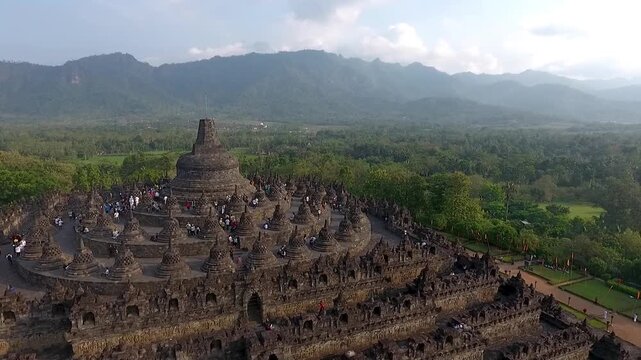 Aerial Orbit Medium Shot of Borobudur Temple with Scenic Mountain Background Under Partly Cloudy Sky in 4K. Cinematic Medium aerial drone view of the Borobudur Temple in Indonesia. The ancient Buddhis