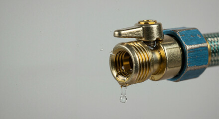 Close-up of a brass water valve leaking a drop. Dripping tap with hose connection on grey background. Plumbing repair and water conservation concept. Copy space