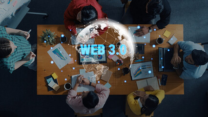 Aerial view of a diverse team collaborating on Web 3.0 strategies at a conference table with laptops, charts, and global networking representation in a modern workspace. Trope