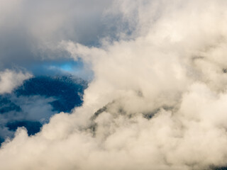 Clouds Veil Snowy Mountain Peaks Under Blue Sky in Misty, Dreamy Skyscape View