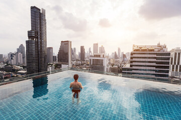 man in rooftop infinity pool in Bangkok city, tourist relaxing in swimming pool with the view of skyscraper buildings, Thailand