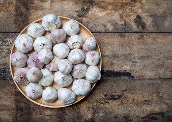 Top view of organic garlic bulbs in a wooden plate with copy space on rustic wood background.