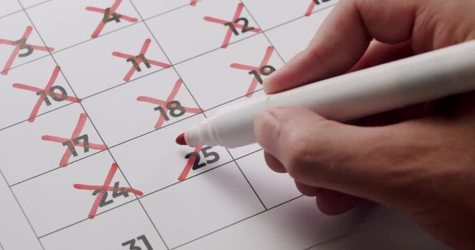 Close-up of a person crossing out days on a calendar, indicating a countdown or scheduling. Person Marking Days Off on a Calendar with a Red Pen for a Countdown