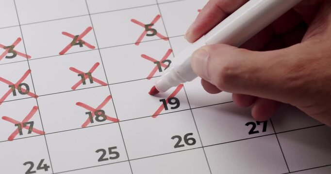 Hand using red marker to cross off dates on a calendar, representing deadline, countdown, or scheduling concept. Hand Crossing Off Days On Calendar, Deadline Or Countdown Concept