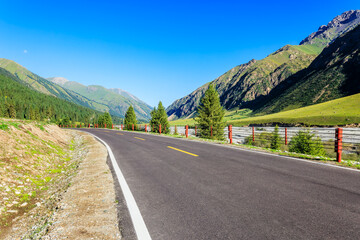 Fototapeta premium Empty asphalt road winding through green mountains and valley under clear blue sky in summer