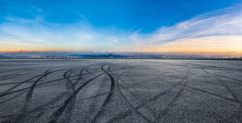Empty asphalt square with tire tracks and city skyline landscape at sunrise
